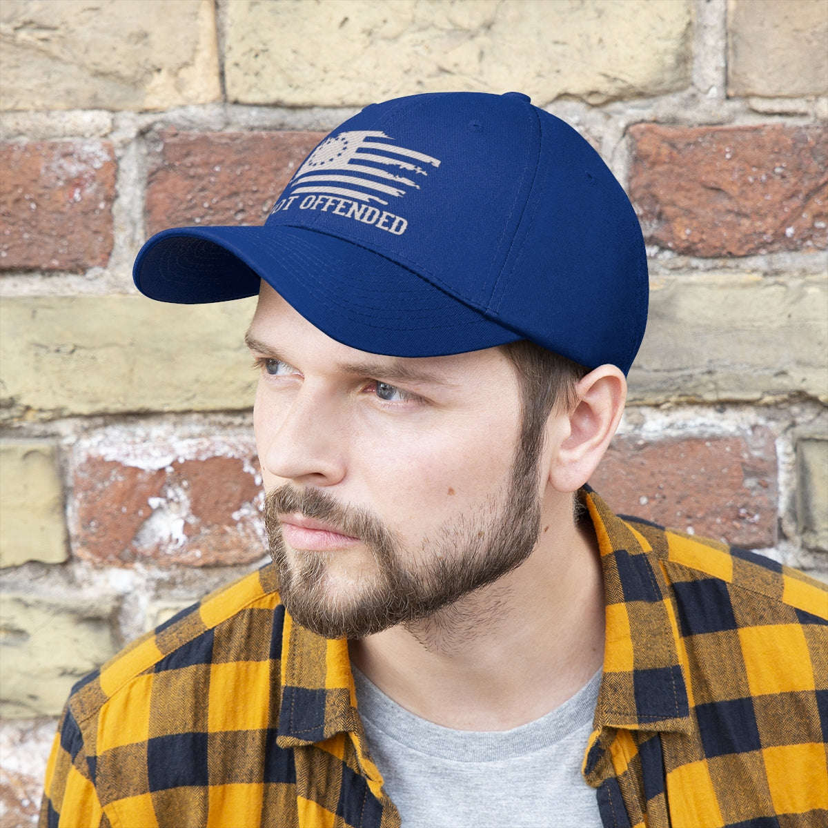 Man wearing an Embroidered Not Offended Adjustable Twill Cap with a classic design against a brick wall.