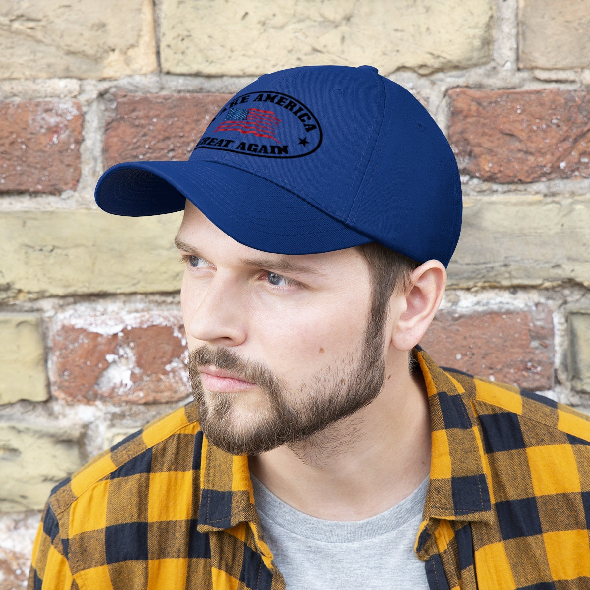 Make America Great Again US Flag Twill Cap worn by a man with a beard and plaid shirt against a brick wall.