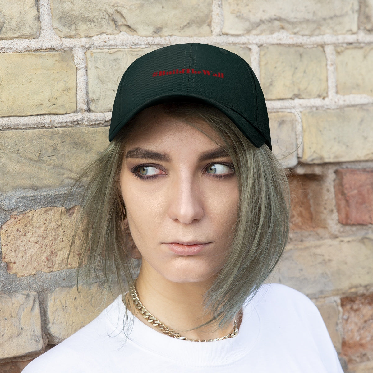 Build The Wall Embroidered Cotton Twill Cap worn by a young woman against a brick wall background.