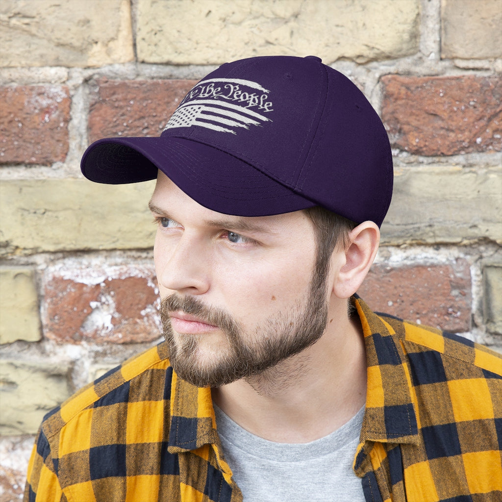 We The People On Distressed American Flag Twill Cap worn by a man in casual attire against a brick wall background.