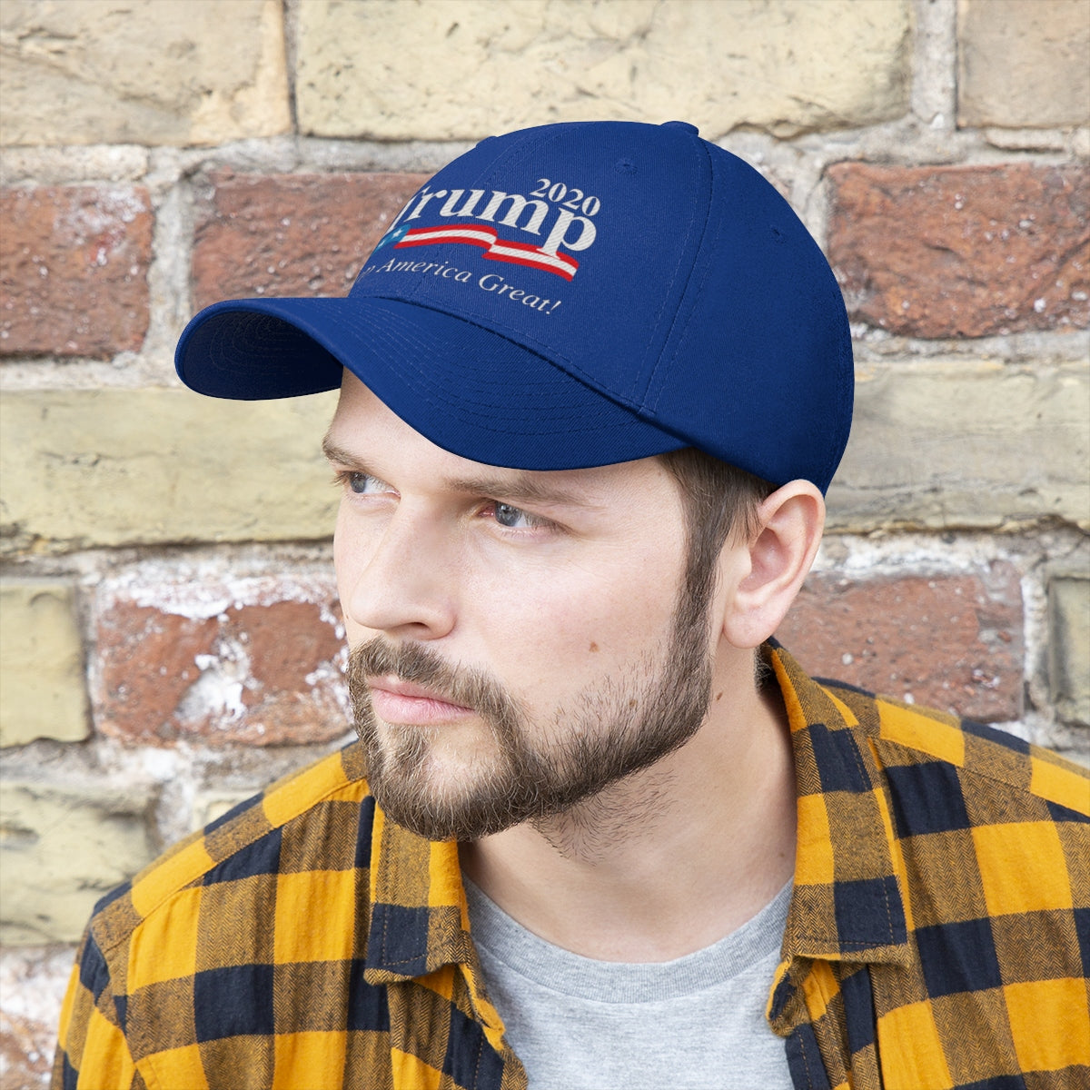 Man wearing Trump 2020 Keep America Great Twill Cap against a brick wall, showcasing patriotic style.