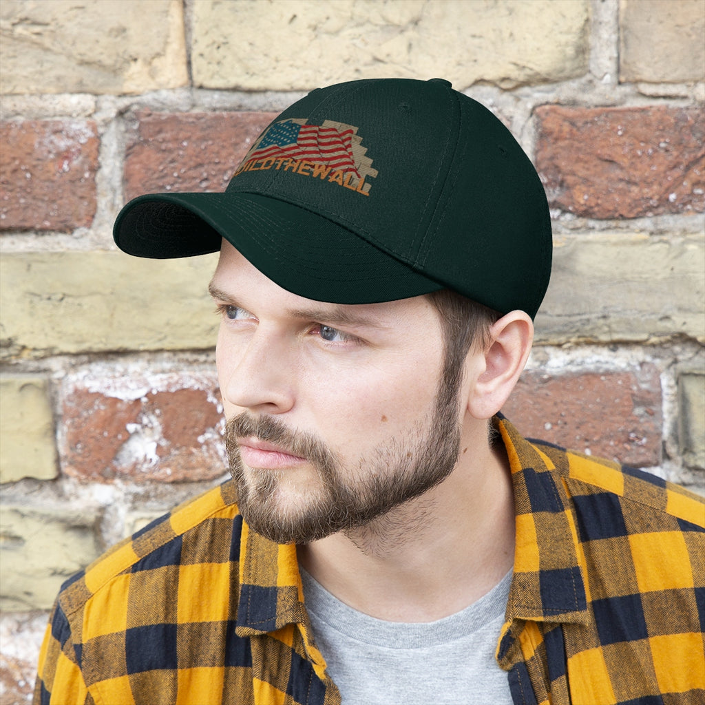 Build The Wall On American Flag Twill Cap worn by a man with a beard, set against a rustic wall.