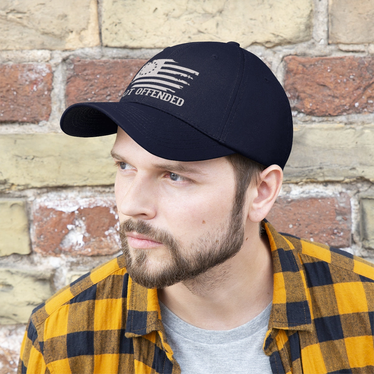 Man wearing Embroidered Not Offended Adjustable Twill Cap against brick wall background.