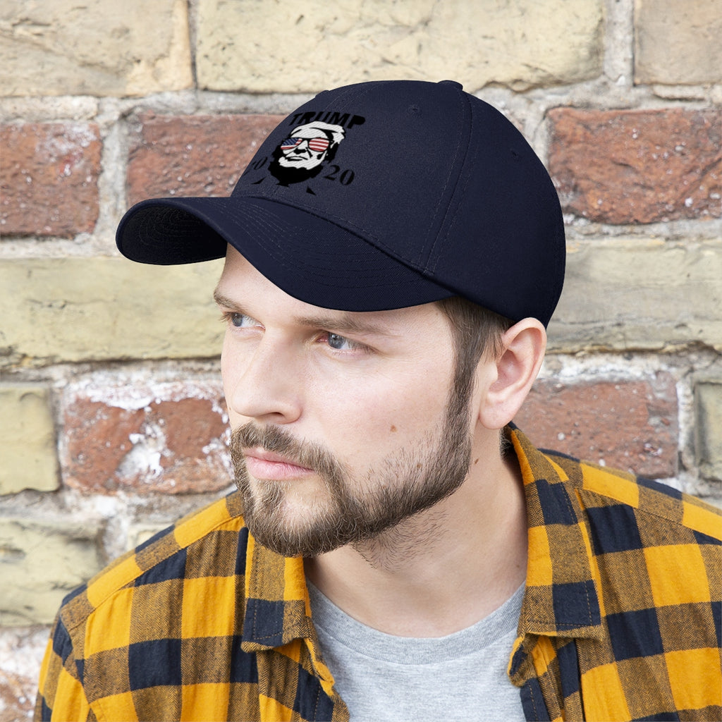 Trump 2020 With US Flag Glasses Twill Cap shown on a man wearing a plaid shirt against a brick wall.