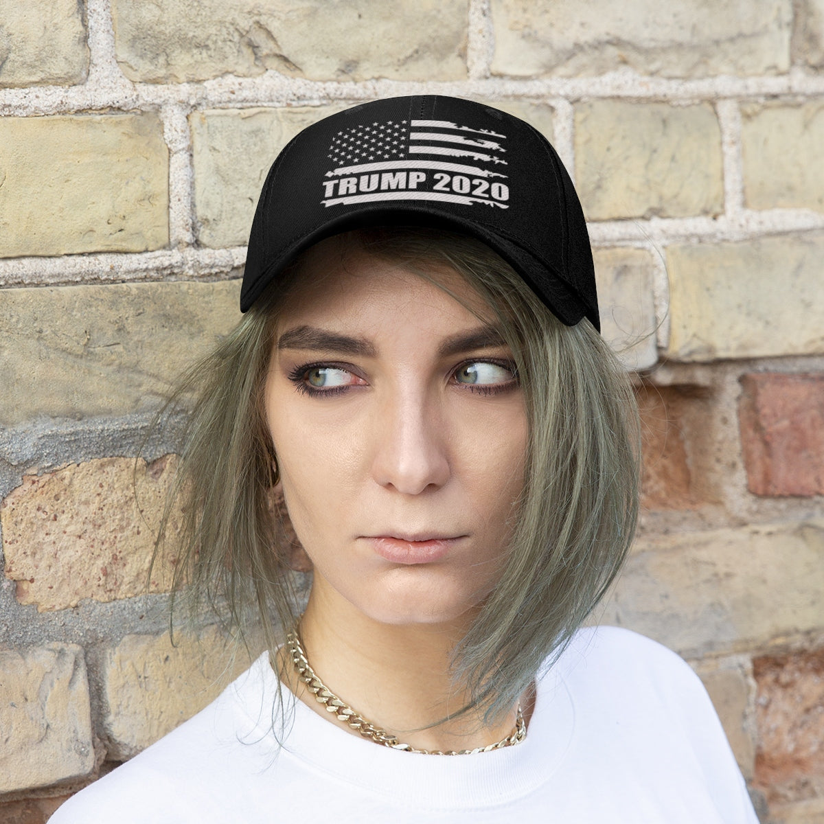 Trump 2020 Distressed American Flag Wht Ltrs Twill Cap worn by a person with short hair against a brick wall.