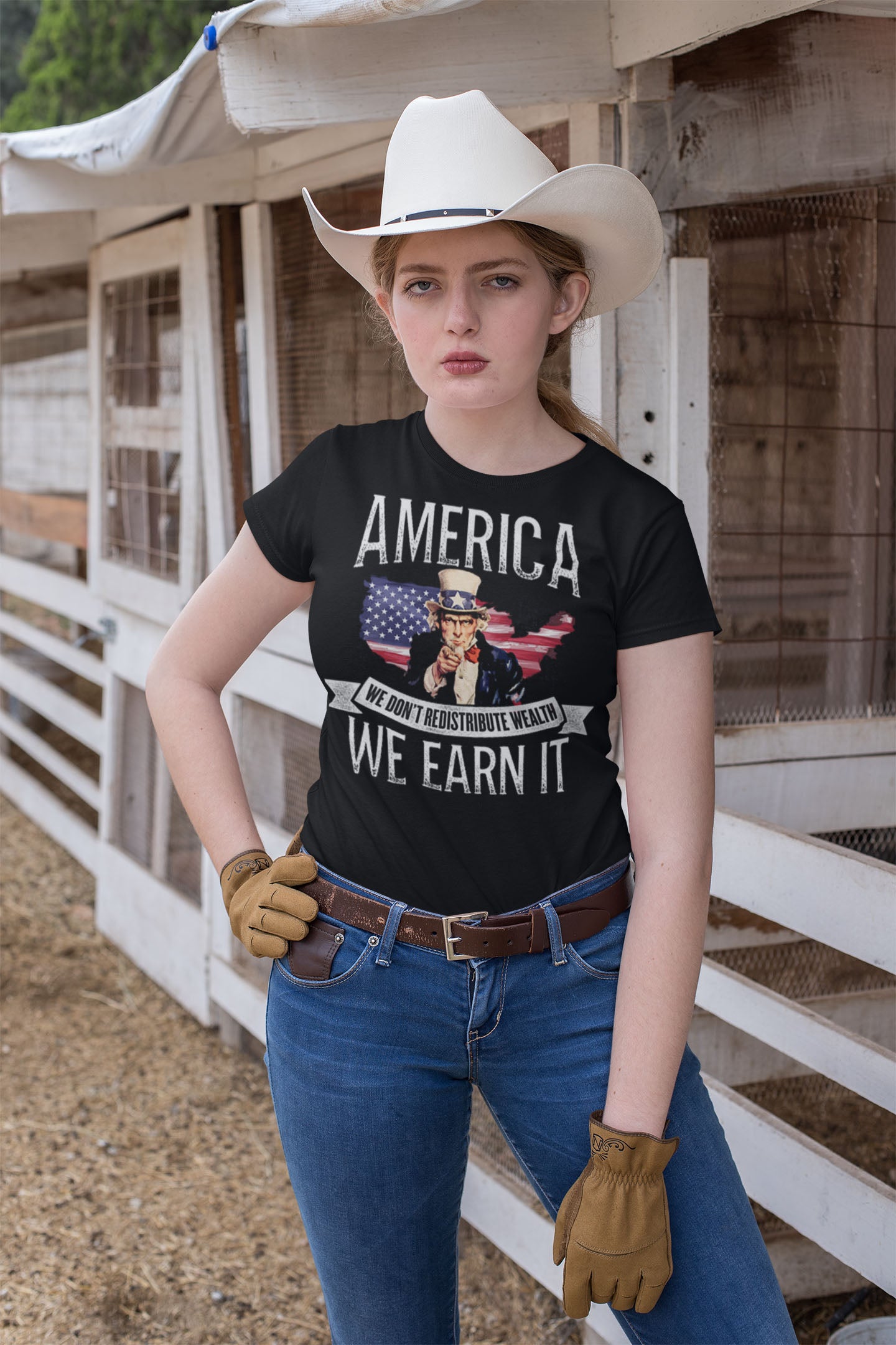 Woman wearing 'We Earn It America Statement Shirt' in a rustic setting
