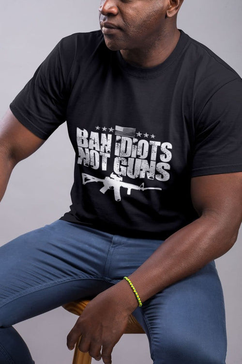 Man wearing a black t-shirt with 'Ban Idiots Not Guns With AR-15' message supporting conservative views, seated on a stool.