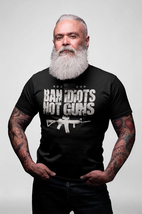 Man wearing a 'Ban Idiots Not Guns With AR-15' shirt with a conservative message, standing confidently with a white beard and tattoos.
