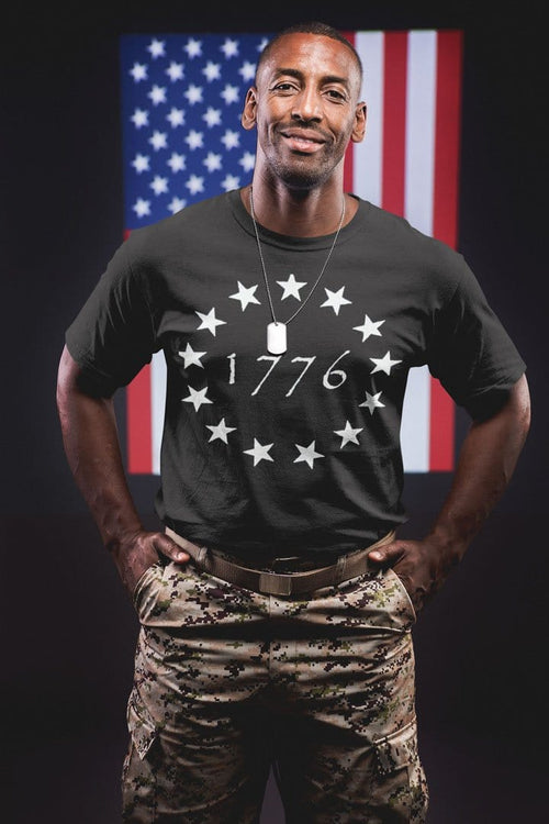 Man wearing Betsy Ross 1776 Stars Vintage American Flag Tee Shirt, standing in front of a U.S. flag.