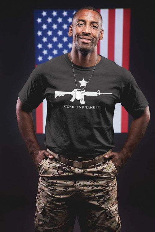 Man wearing Come And Take It AR-15 And Star t-shirt, standing in front of American flag, symbolizing liberty and resistance.