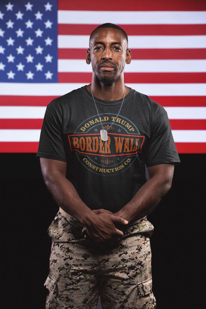 Man wearing Border Wall Graphic Statement Tee in front of American flag