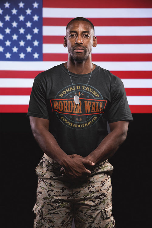 Man wearing Border Wall Graphic Statement Tee in front of American flag