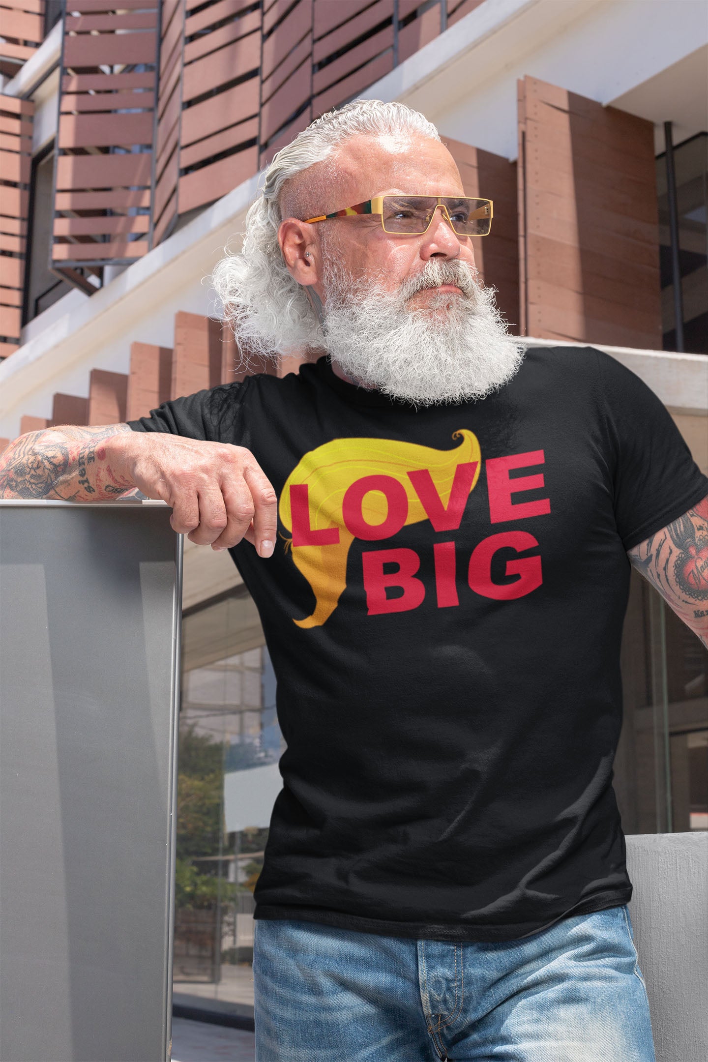 Man wearing Love Big With Trump Hair 2 Red shirt, standing outdoors with modern background