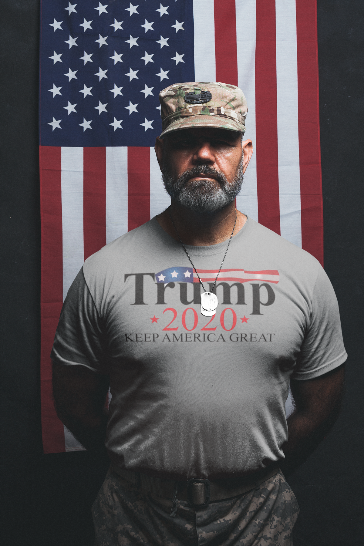 Man in military attire posing in front of an American flag wearing Keep America Great 2020 Twill Cap for Trump.