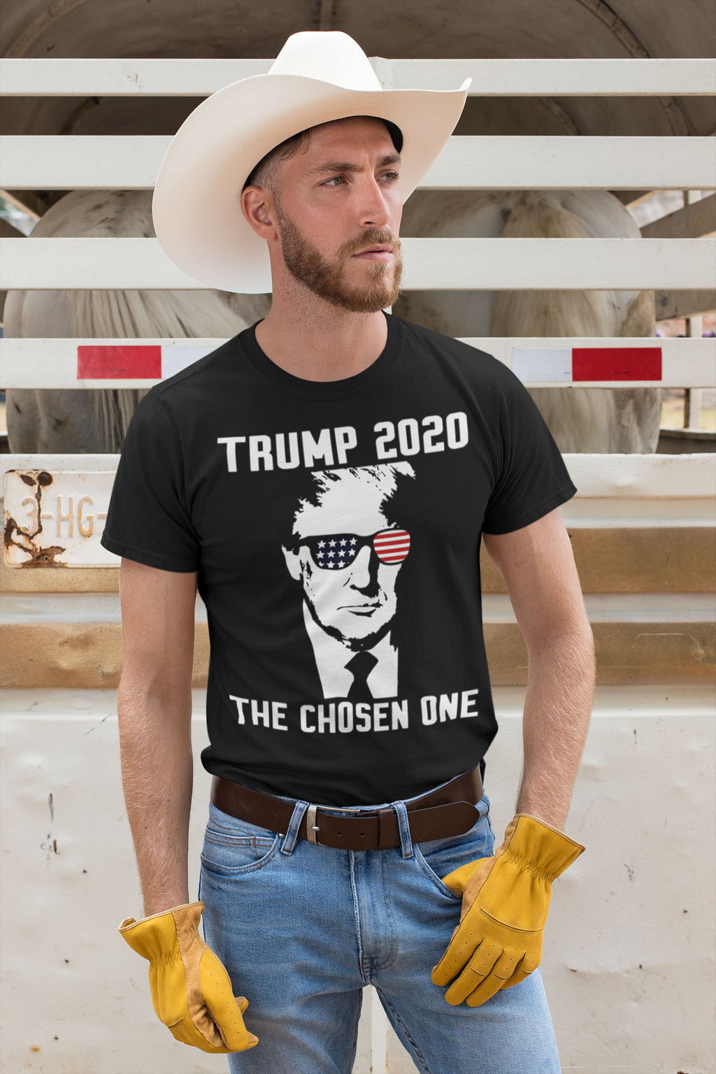 Man wearing Trump 2020 The Chosen One USA Shirt, cowboy hat and gloves, standing near horses.