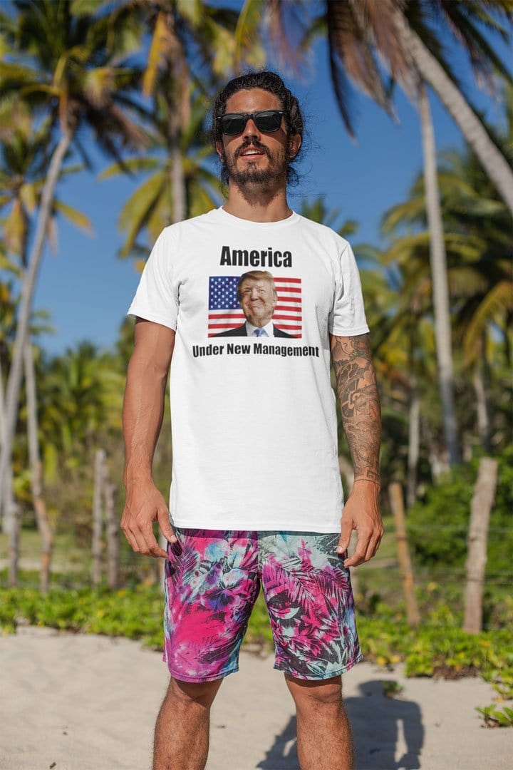 Man wearing America Under New Management Flag Featuring Trump shirt standing on beach.