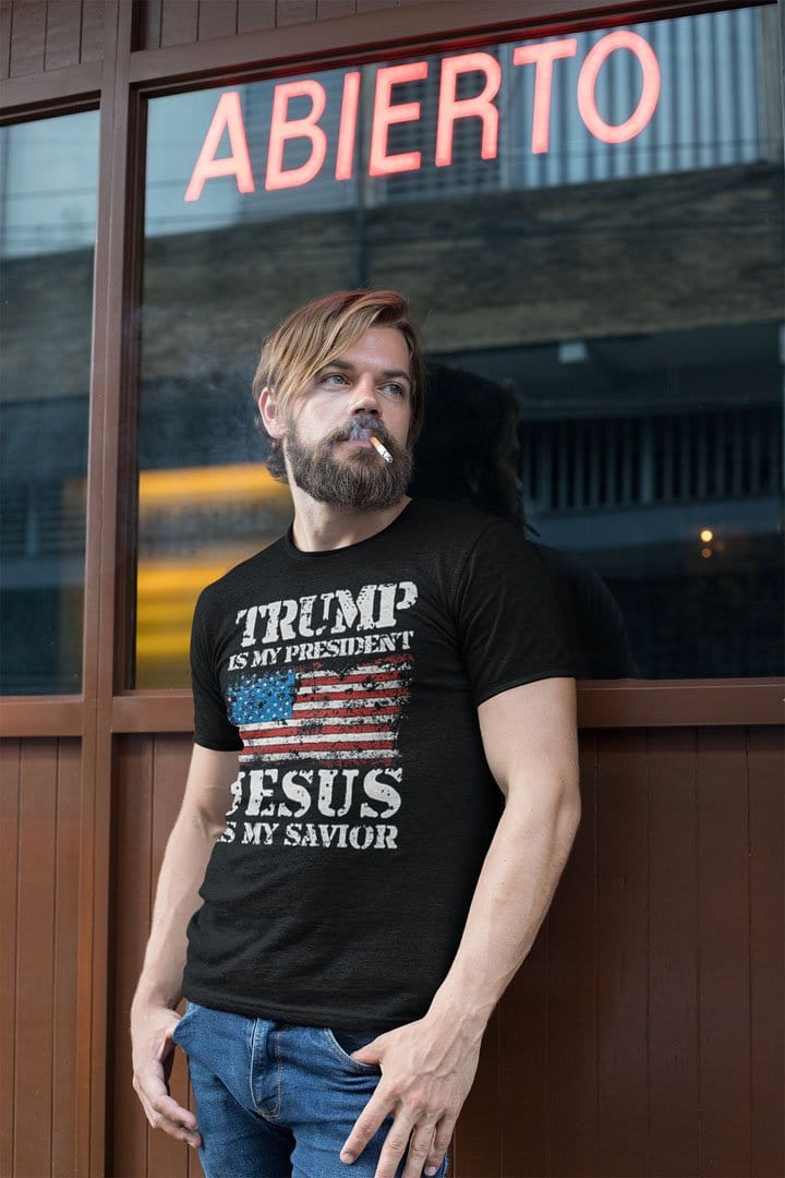 Man wearing 'Trump Is My President Jesus Is My Savior' shirt standing outside a cafe.