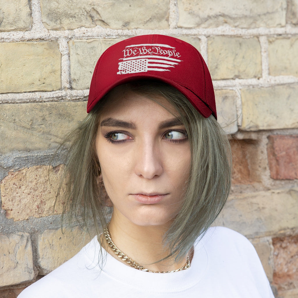 We The People On Distressed American Flag Twill Cap worn by a model against a rustic brick background.