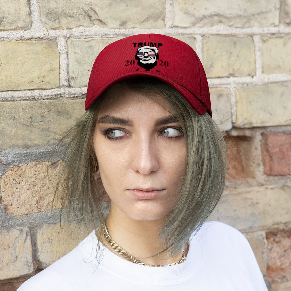 Trump 2020 With US Flag Glasses Twill Cap worn by woman with green hair, against brick wall.