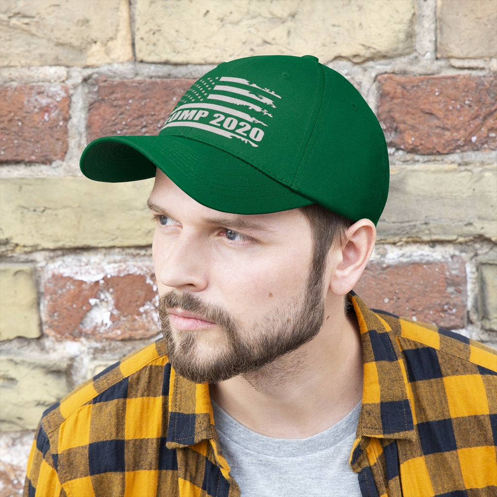 Trump 2020 Distressed American Flag Wht Ltrs Twill Cap worn by a man in a plaid shirt against a brick wall.