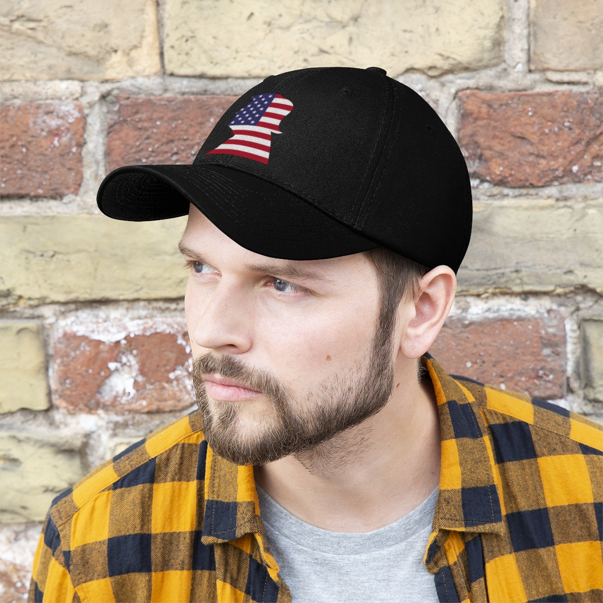 Trump American Flag SilhouetteTwill Cap worn by a man with a beard, set against a brick wall background.