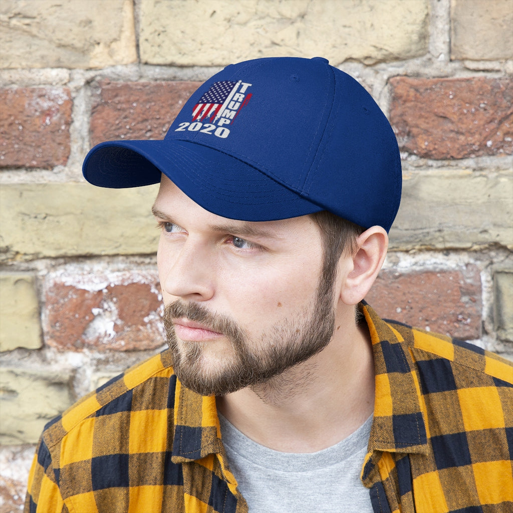 Vertical Distressed American Flag 2020 Trump Twill Cap worn by a man against a brick wall.