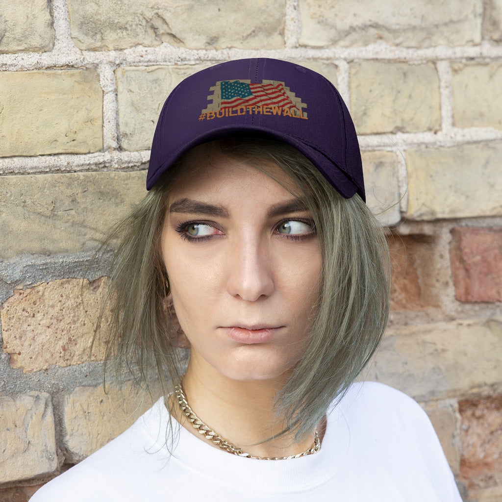 Build The Wall On American Flag Twill Cap worn by a model against a brick background, showcasing its bold design.