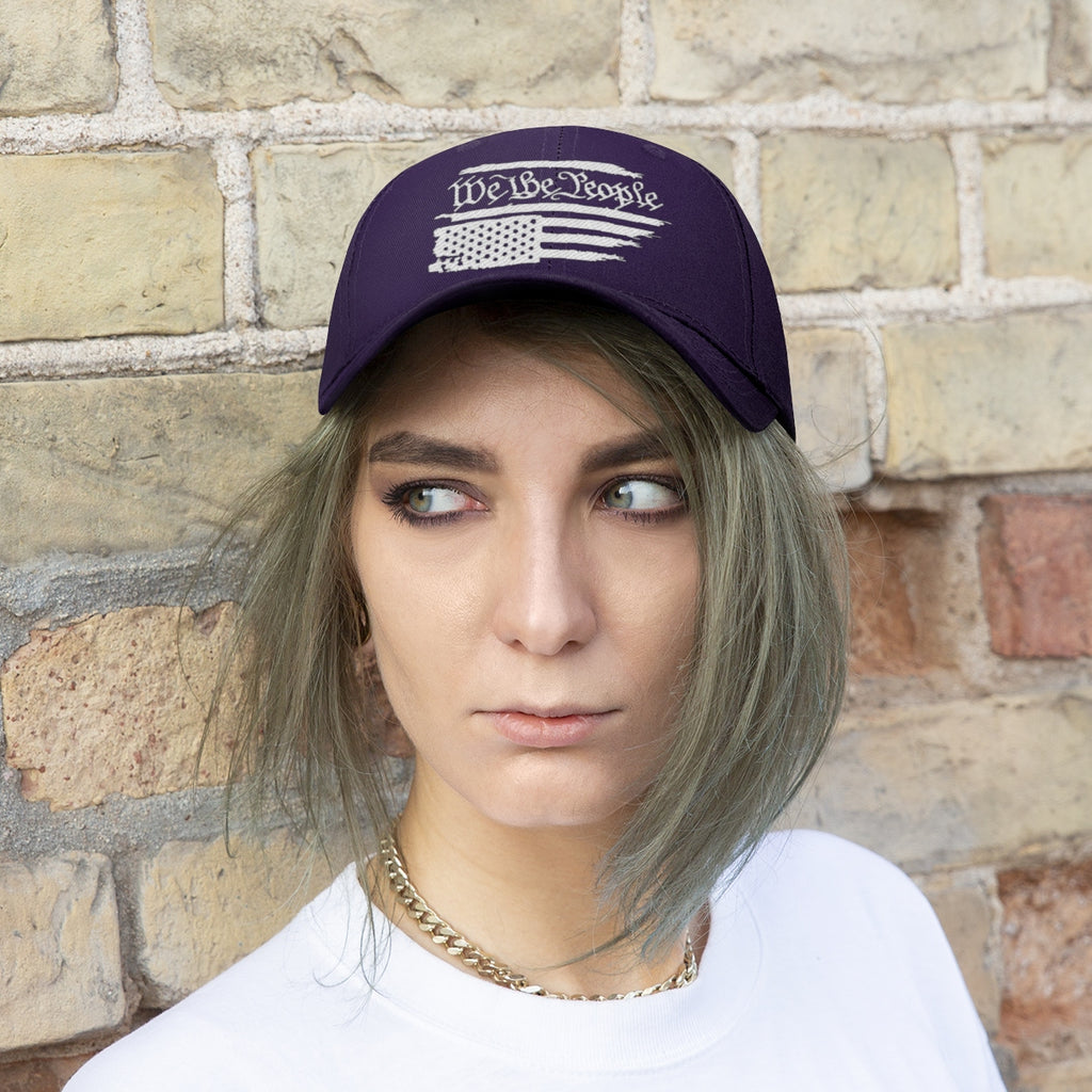 We The People On Distressed American Flag Twill Cap worn by a person with short hair in front of a brick wall.