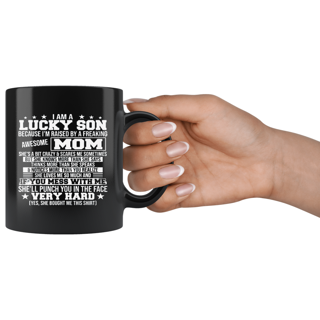 Black ceramic mug with the text 'Lucky Son Raised By An Awesome Mom' held in hand, high gloss finish, perfect for hot and cold drinks.