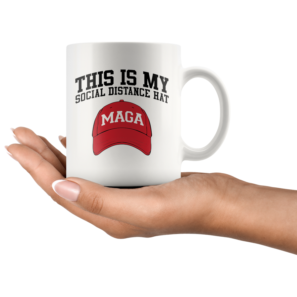 Hand holding a mug with 'This Is My Social Distance Hat MAGA' and red MAGA hat design.