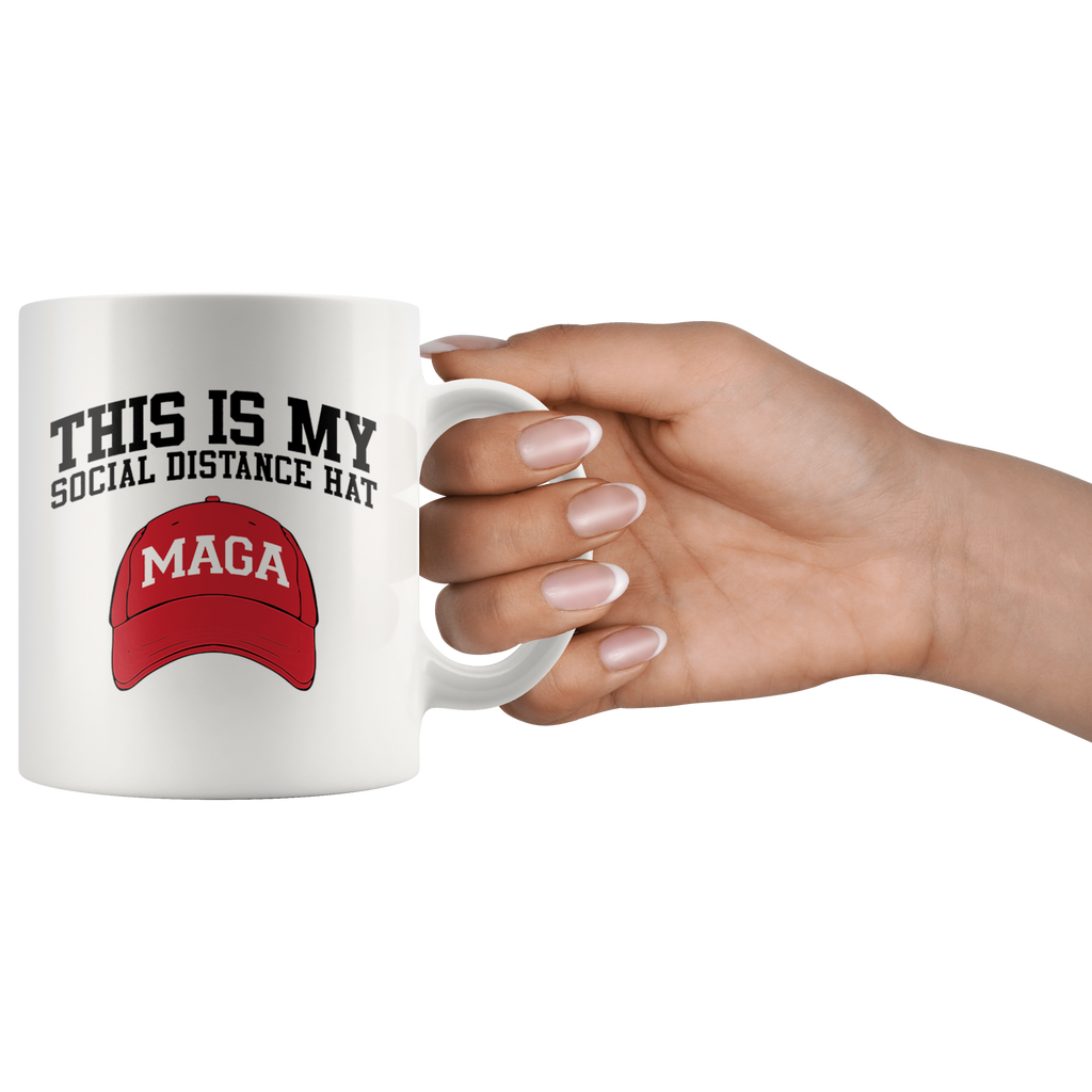 Hand holding a mug with 'This Is My Social Distance Hat MAGA' design featuring a red MAGA hat graphic